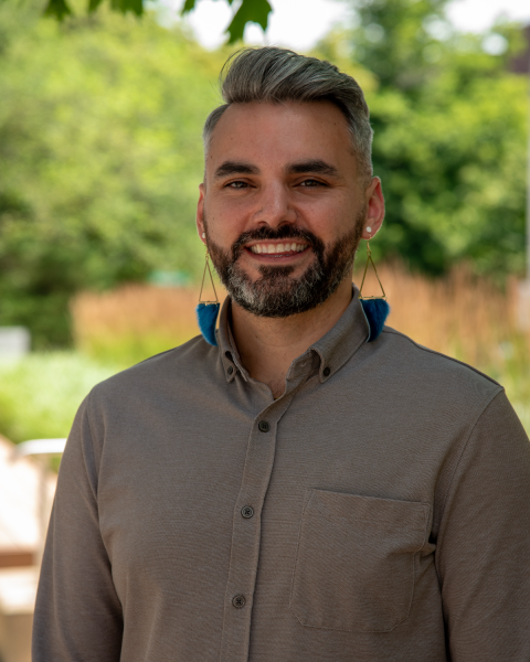 Headshot of a smiling man with a salt and pepper hair and a dark beard and mustache