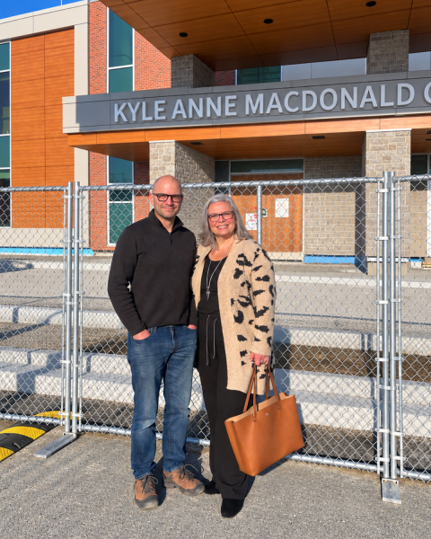 Image of a man (left) and woman (right) standing in front of a building and a construction fence.