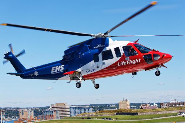 Close up image of an EHS helicopter with blue sky and buildings in the foreground.